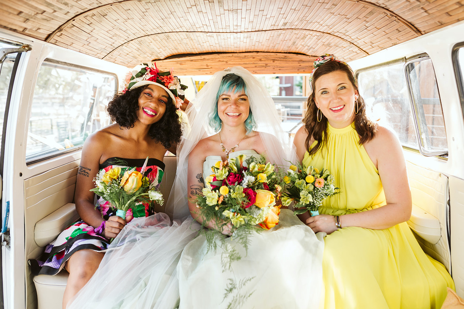 bride with colorful bouquet sits between two women in bright gowns in VW bus at Chattanooga lesbian wedding styled shoot