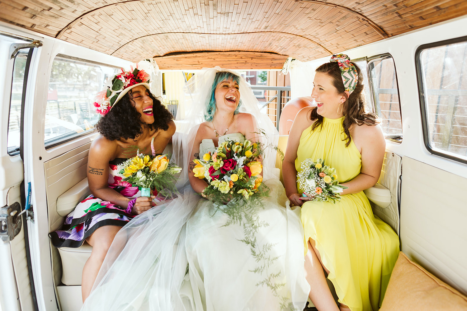 bride with colorful bouquet sits between two women in bright gowns in VW bus at Chattanooga lesbian wedding styled shoot