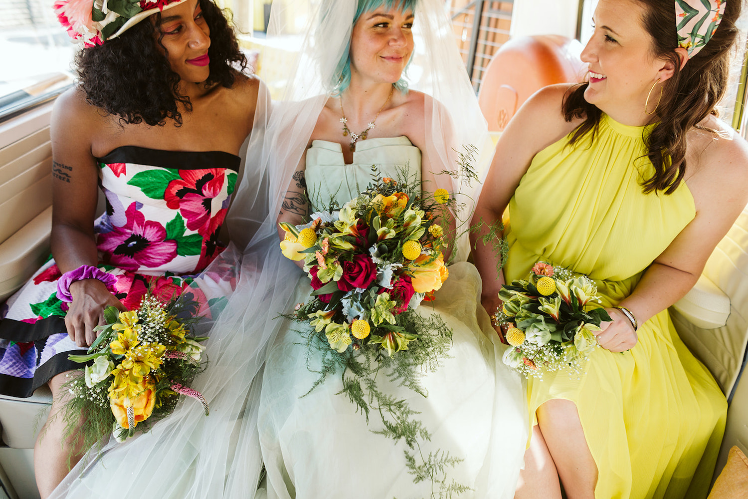 bride with colorful bouquet sits between two women in bright gowns in VW bus at Chattanooga lesbian wedding styled shoot