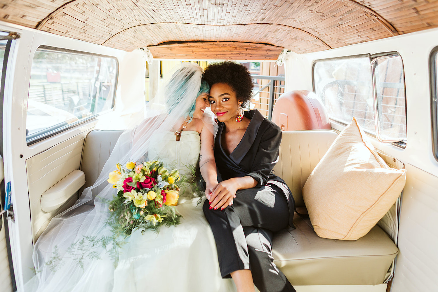 two brides at LGBTQ wedding in Chattanooga styled shoot wear a strapless white gown and black pantsuit in back of VW bus