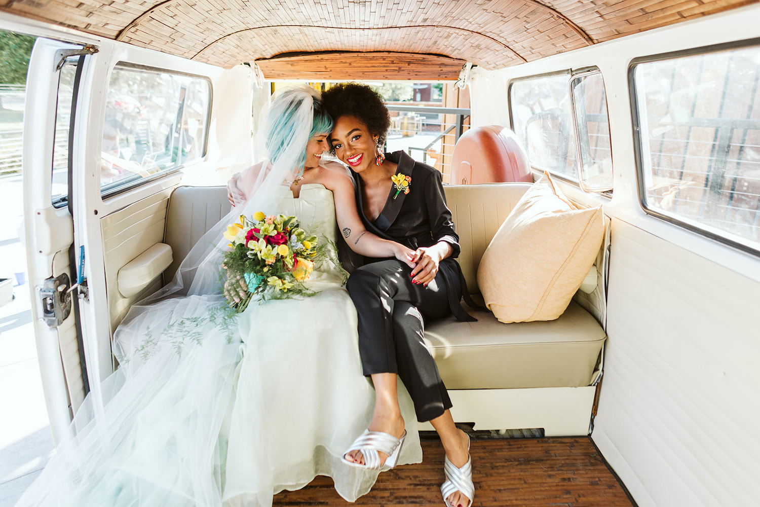 two brides at LGBTQ wedding in Chattanooga styled shoot wear a strapless white gown and black pantsuit in back of VW bus