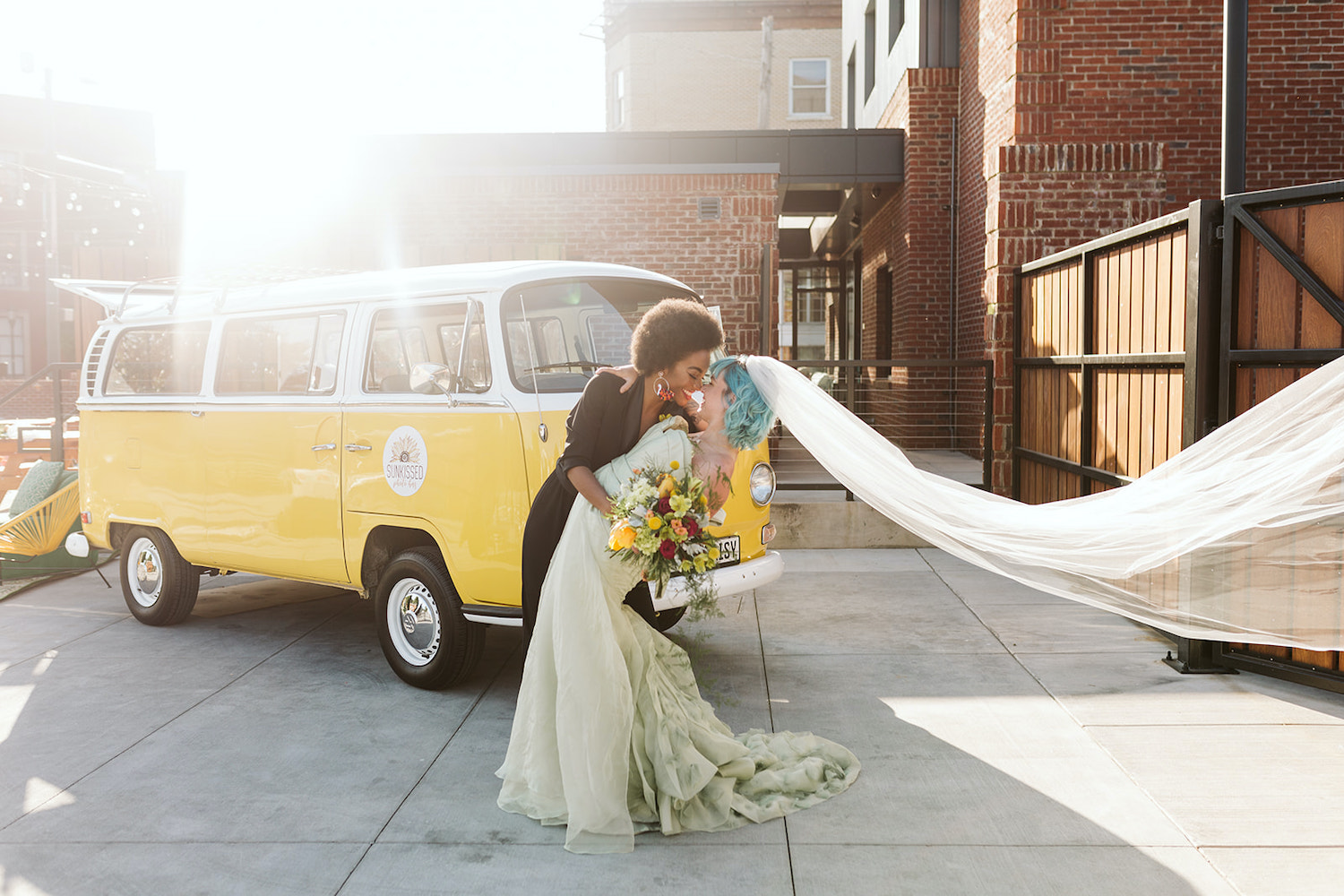 bride in black pantsuit hugs bride in strapless white gown at LGBTQ wedding in Chattanooga in front of yellow Volkswagon bus