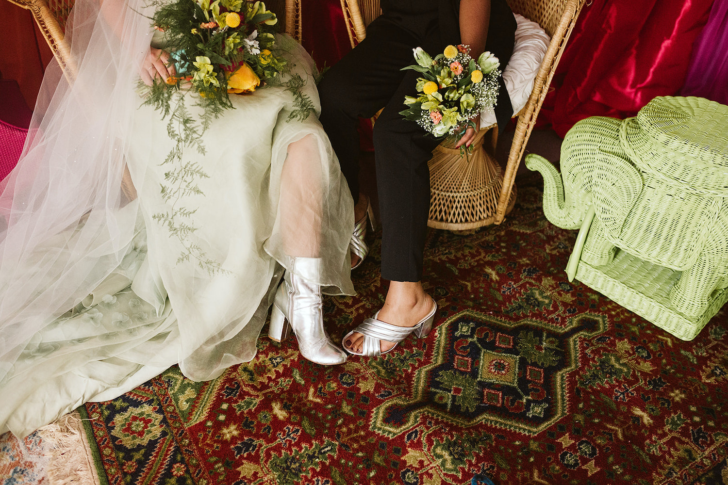 lesbian couple sits on peacock rattan chairs in front of bright wall draperies at Moxy Hotel at LGBTQ Wedding in Chattanooga