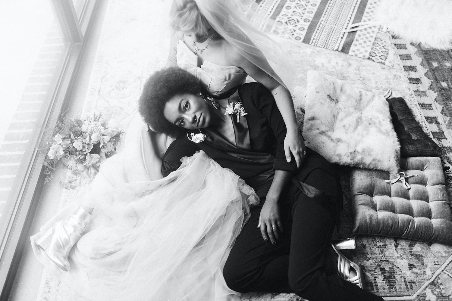 lesbian couple in strapless gown and black pantsuit cuddles on colorful pillows at Moxy Hotel at LGBTQ Wedding in Chattanooga