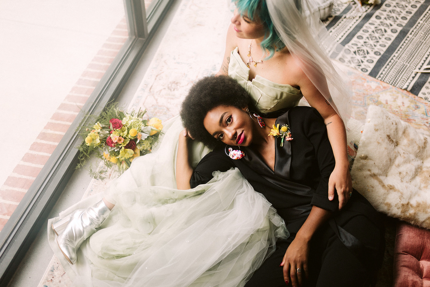 lesbian couple in strapless gown and black pantsuit cuddles on colorful pillows at Moxy Hotel at LGBTQ Wedding in Chattanooga