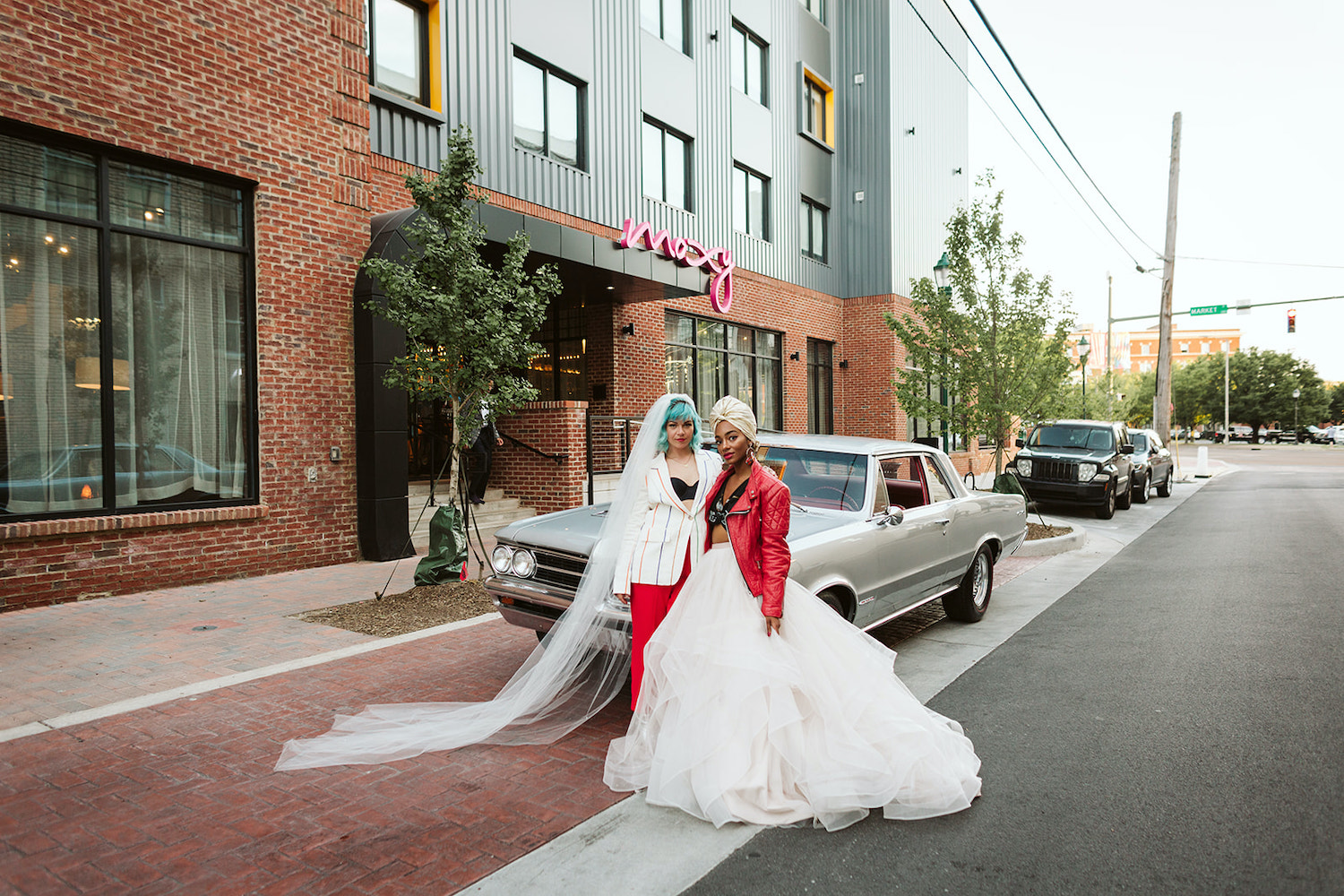 LGBTQ wedding styled shoot in downtown Chattanooga at Moxy Hotel with two brides standing on street in front of vintage car