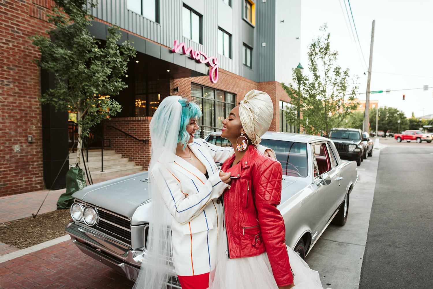 two brides at lesbian wedding styled shoot wearing white dress with red leather jacket and red pants with white jacket