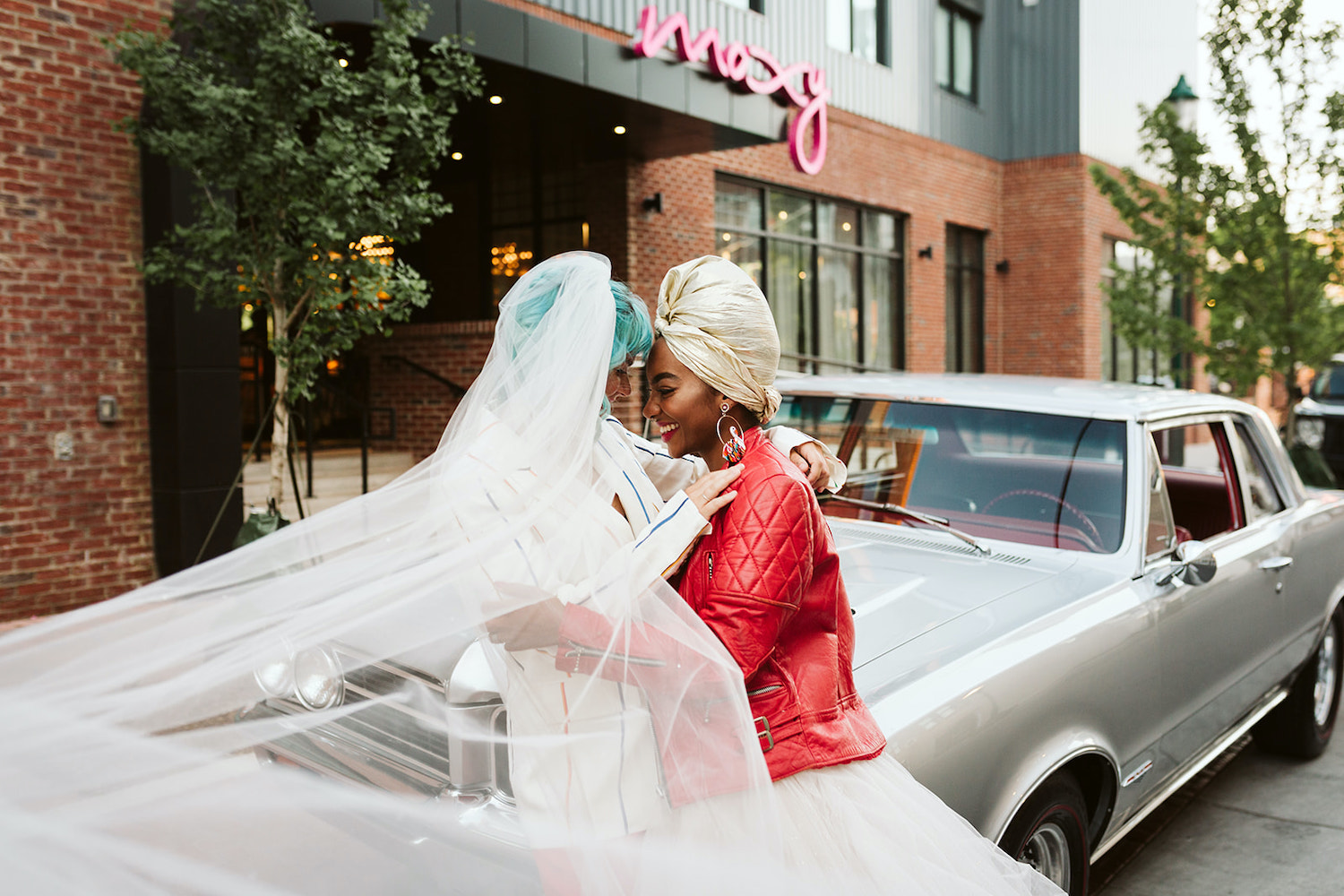 two brides at lesbian wedding styled shoot wearing white dress with red leather jacket and red pants with white jacket