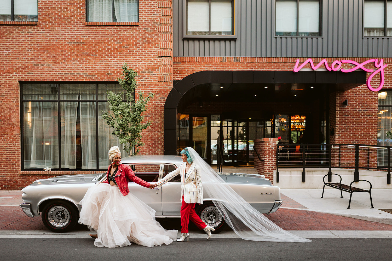 two brides at LGBTQ wedding in Chattanooga styled shoot hold hands on the street in front of vintage car and Moxy Hotel