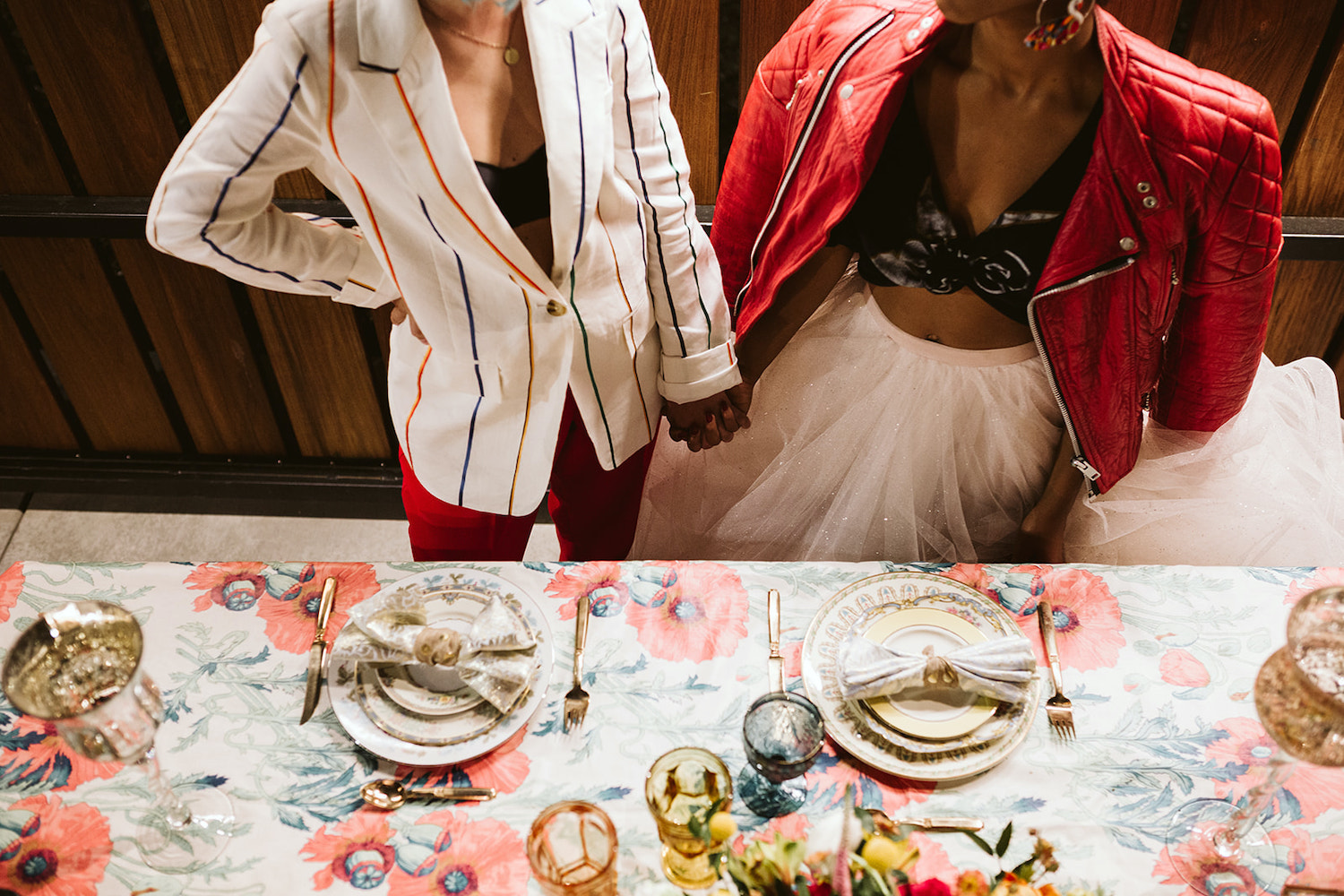 two brides hold hands next to colorfully decorated dinner table