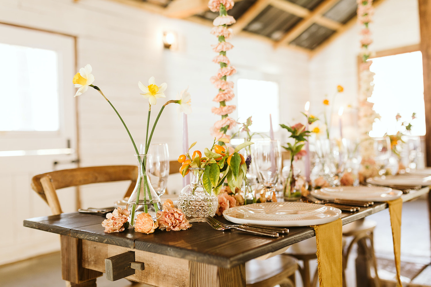 wooden farm table at Oakleaf Cottage wedding set with goldenrod napkins, flatware, white plates, and simple floral arrangements