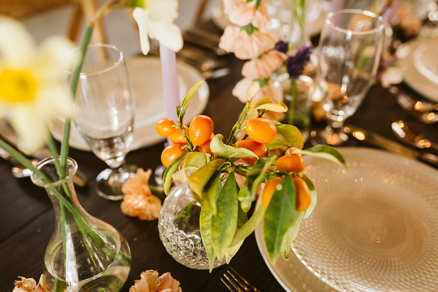 kumquats and greenery in a small clear glass vase set on a wooden farm table