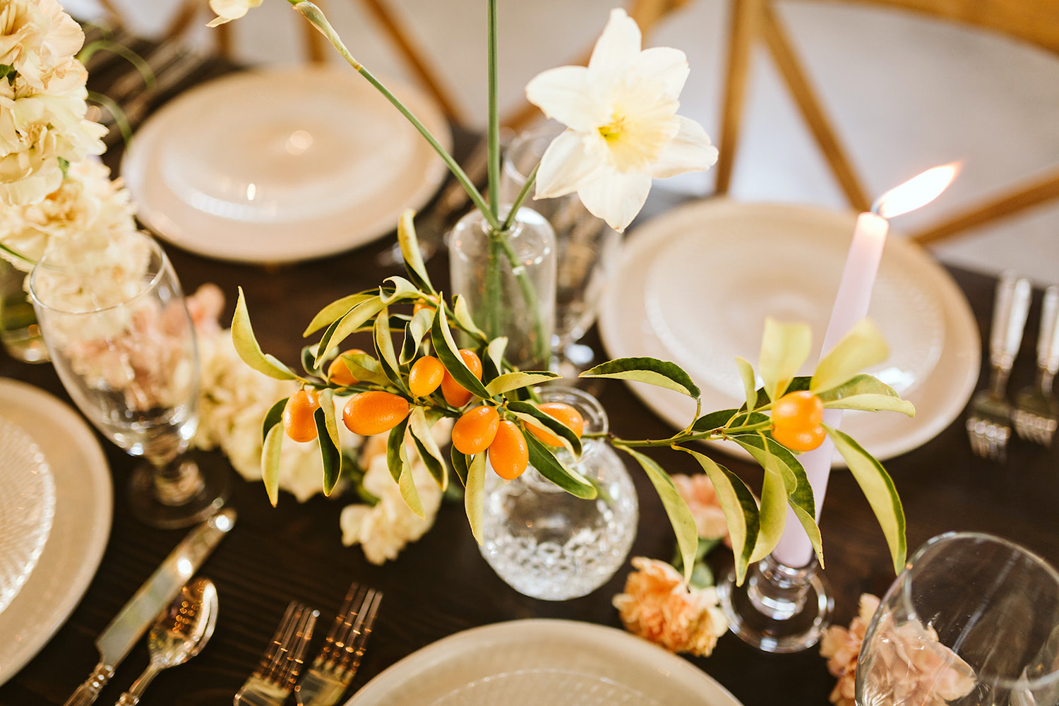 kumquats and greenery in a small clear glass vase set on a wooden farm table