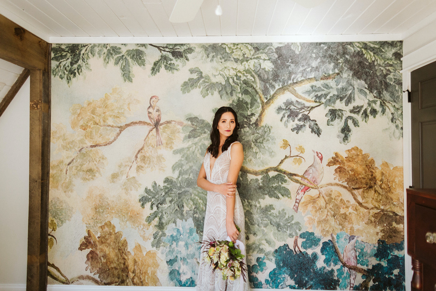 bride wearing embroidered gown stands in front of watercolor wallpapered wall at Oakleaf Cottage wedding