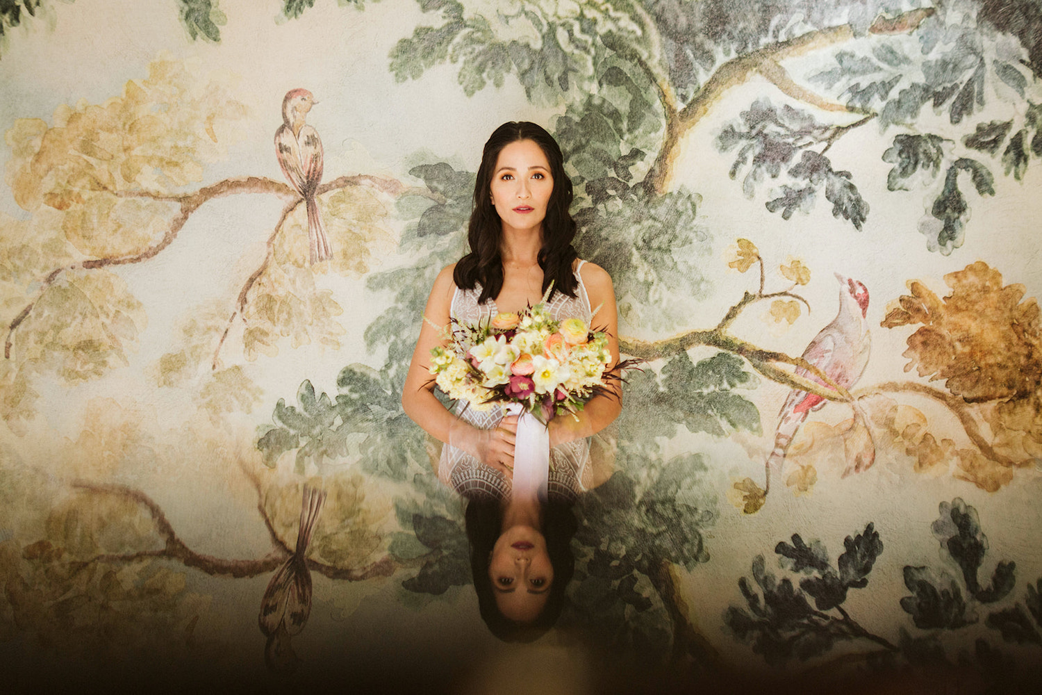 bride wearing embroidered gown stands in front of watercolor wallpapered wall at Oakleaf Cottage wedding