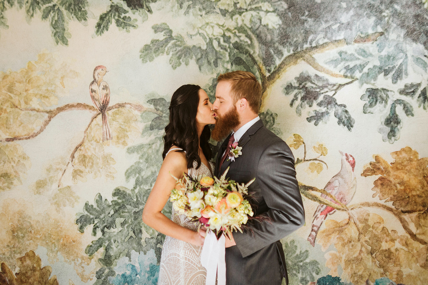 bride and groom kiss in front of watercolor wallpapered wall at Oakleaf Cottage wedding