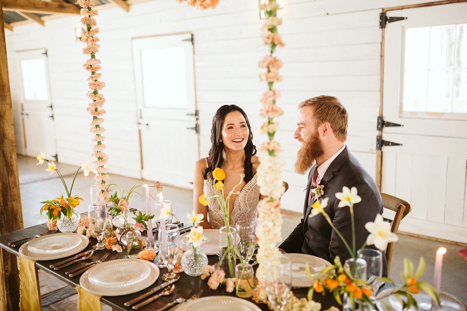 bride and groom laugh sitting at a farm table with simple table settings and florals at Oakleaf Cottage wedding