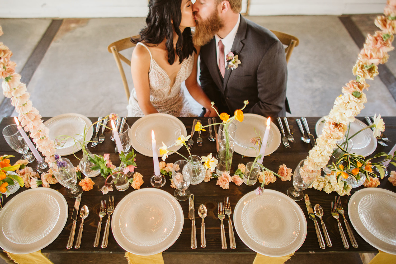 bride and groom kiss while sitting at a farm table with simple table settings and florals at Oakleaf Cottage wedding