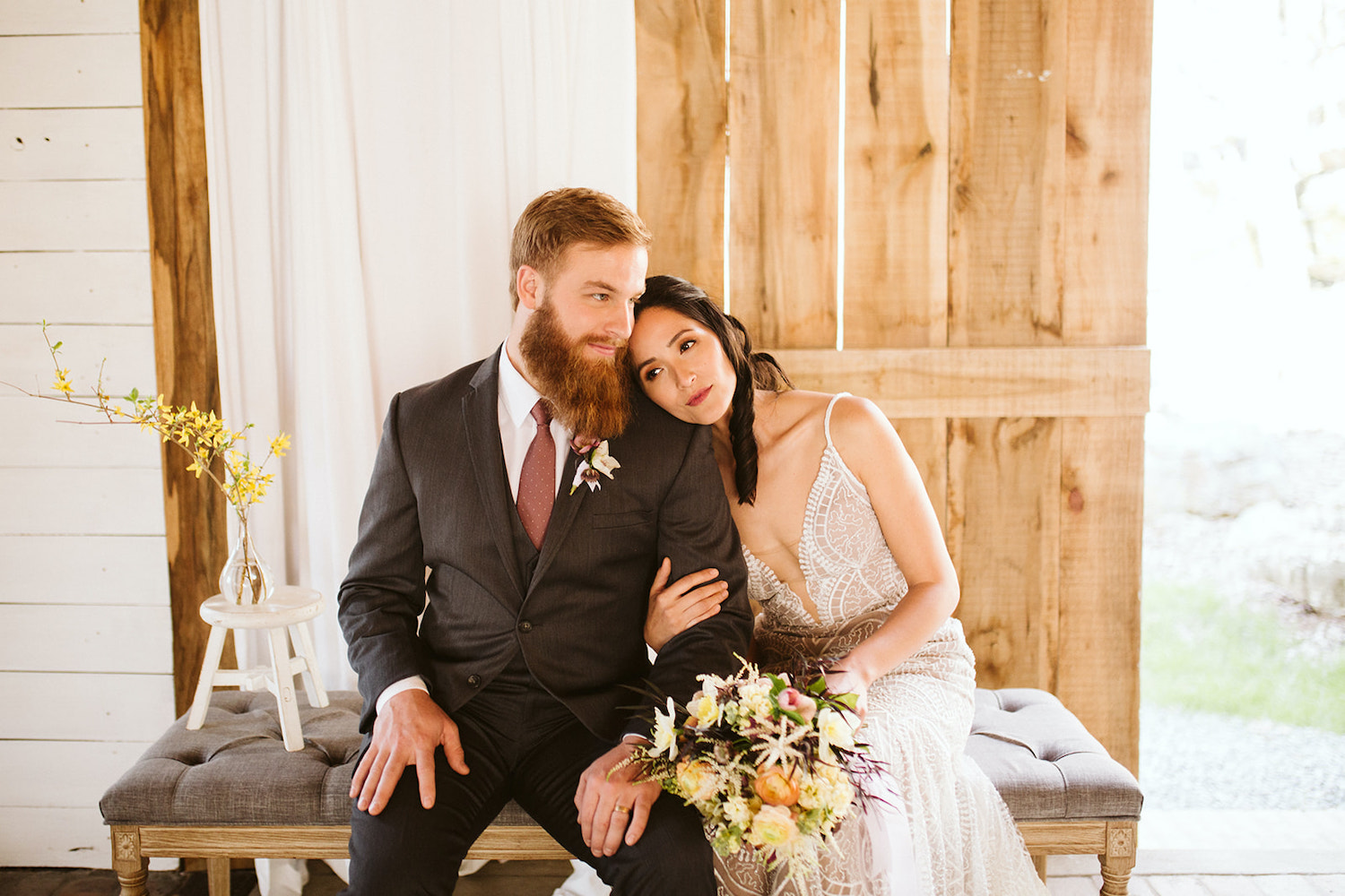 bride and groom sit on a padded bench with her hand holding his arm and her head on his shoulder at Oakleaf Cottage wedding