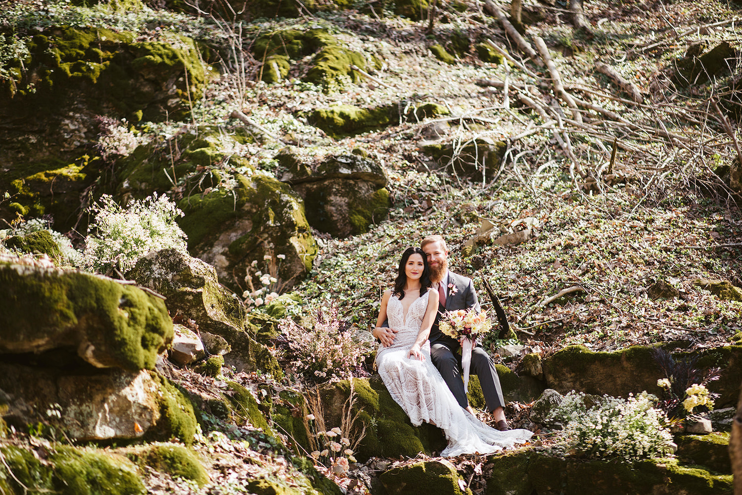 bride and groom sit on mossy boulder in the woods near their Oakleaf Cottage wedding on Lookout Mountain