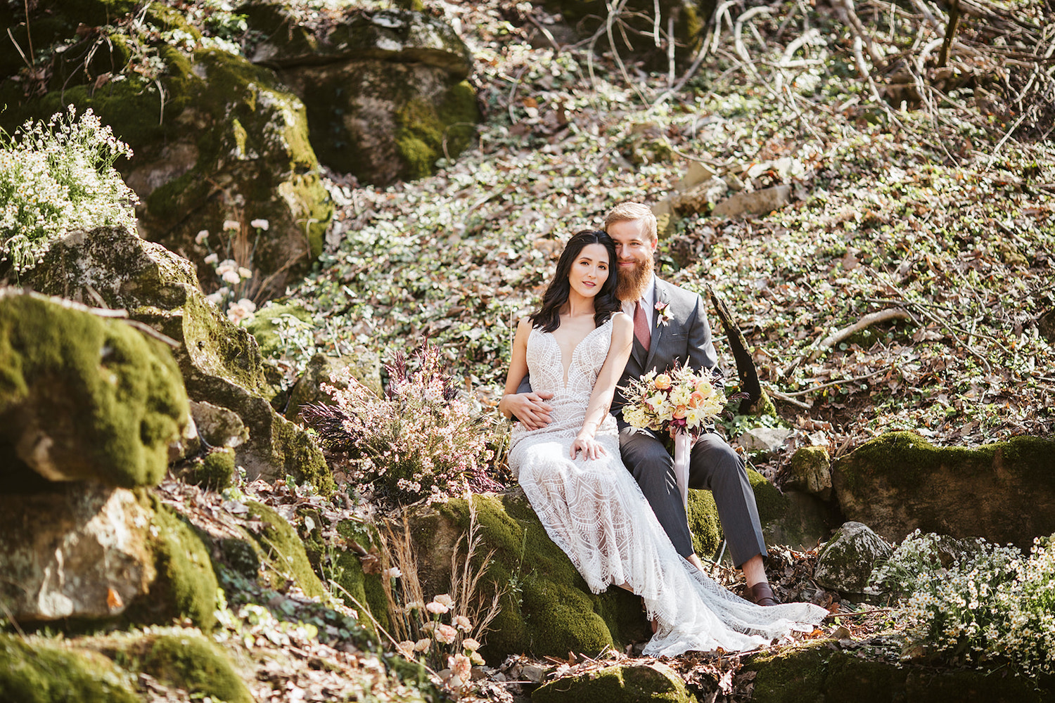 bride and groom sit on mossy boulder in the woods near their Oakleaf Cottage wedding on Lookout Mountain