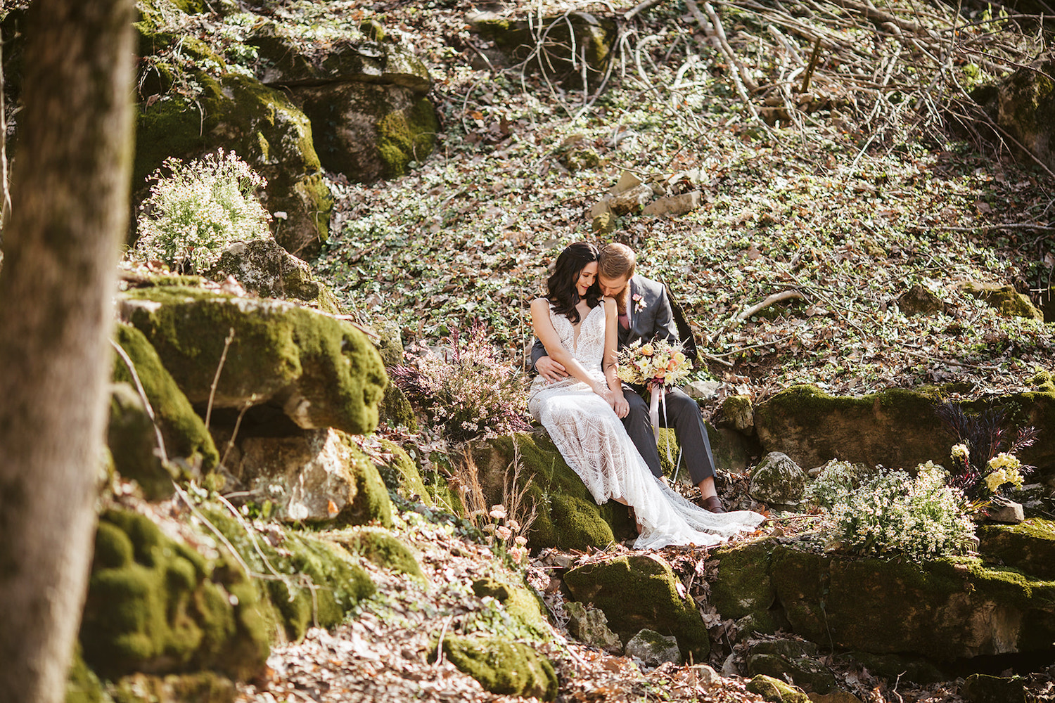 bride and groom sit on mossy boulder in the woods near their Oakleaf Cottage wedding on Lookout Mountain