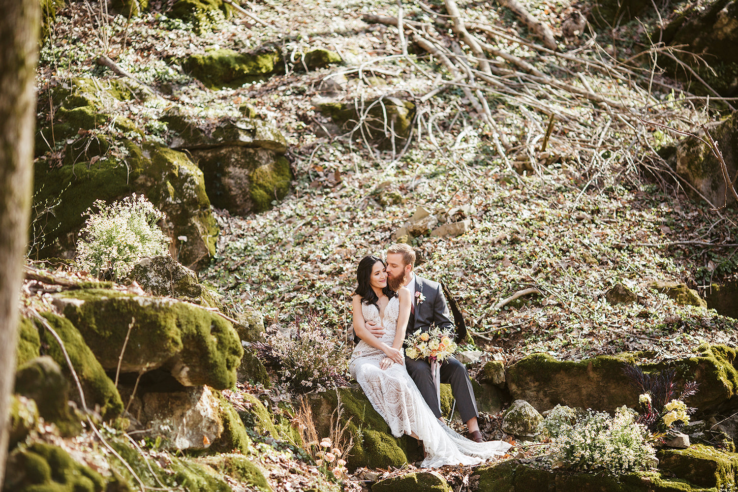 bride and groom sit on mossy boulder in the woods near their Oakleaf Cottage wedding on Lookout Mountain