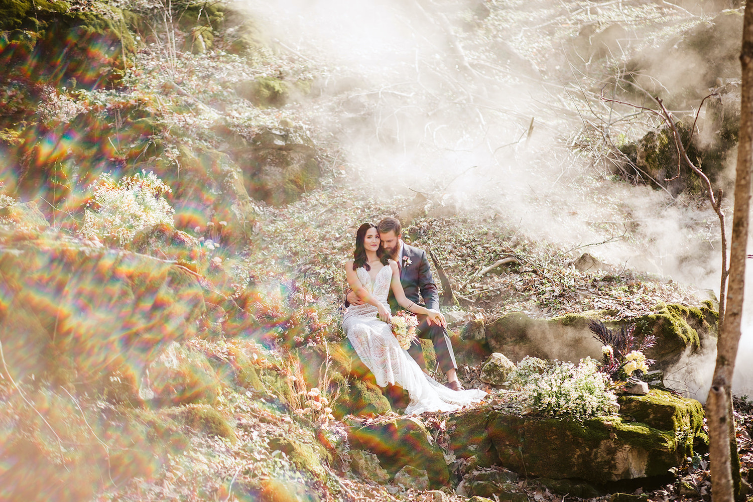 bride and groom sit on mossy boulder in the misty woods near their Oakleaf Cottage wedding on Lookout Mountain