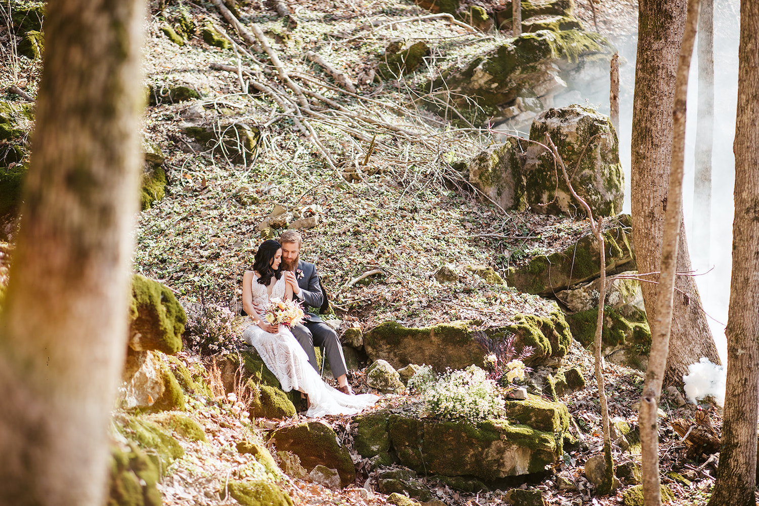 bride and groom sit on mossy boulder in the misty woods near their Oakleaf Cottage wedding on Lookout Mountain