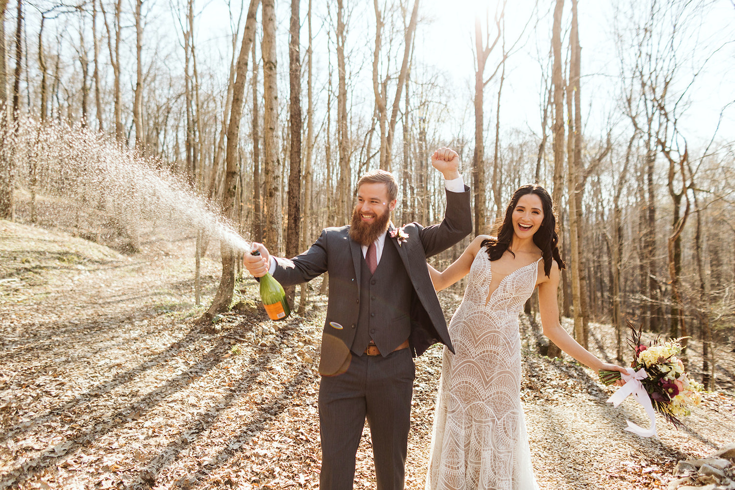 groom sprays bottle of champagne while he and bride laugh together