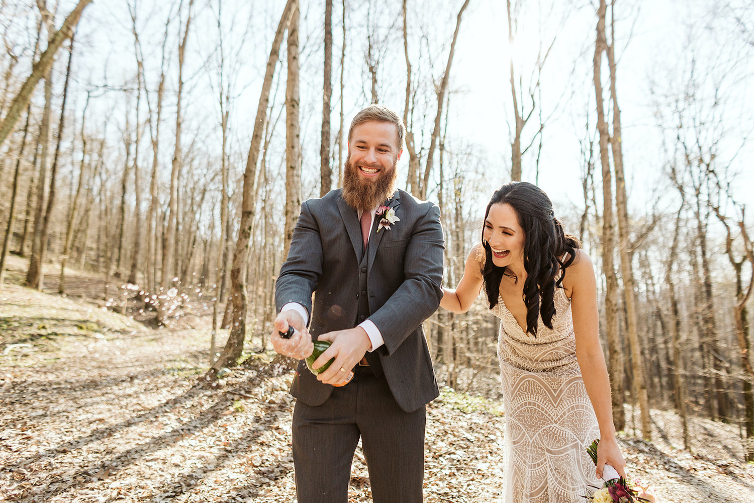 groom shakes bottle of champagne while he and bride laugh together