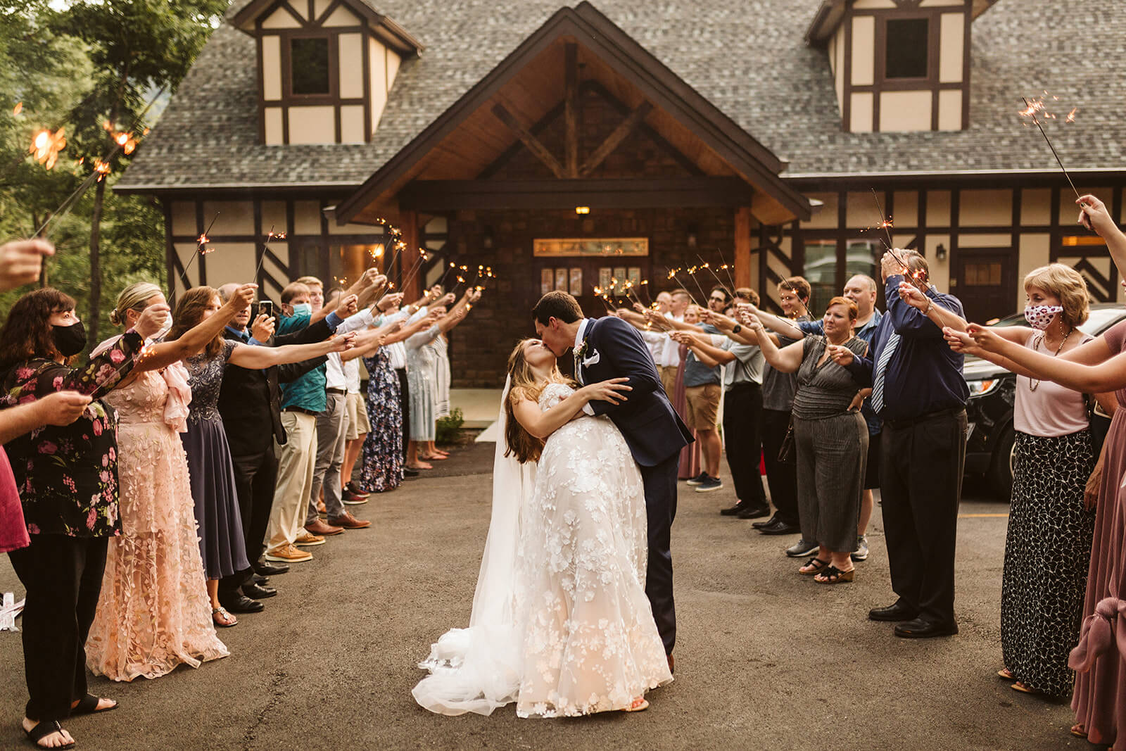 A bride and groom kiss surrounded by guests holding sparklers.