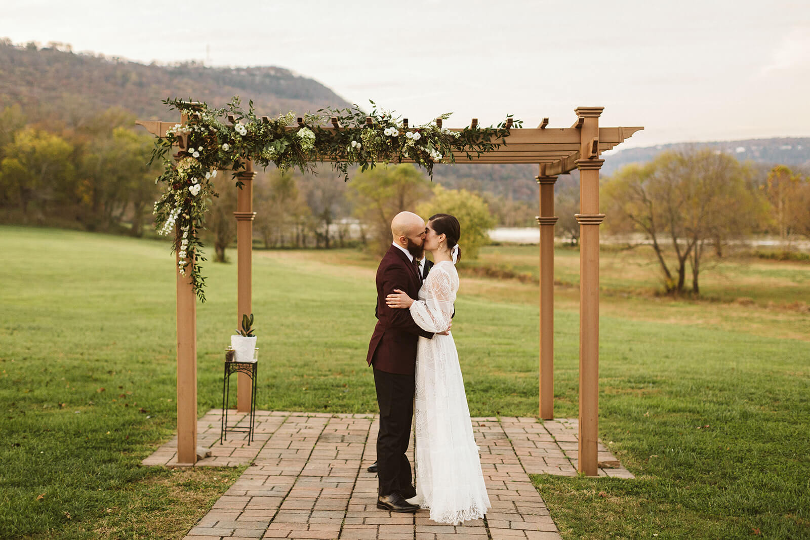 A bride and groom kiss beneath a floral arbor in front of mountains and the river in Chattanooga, TN.