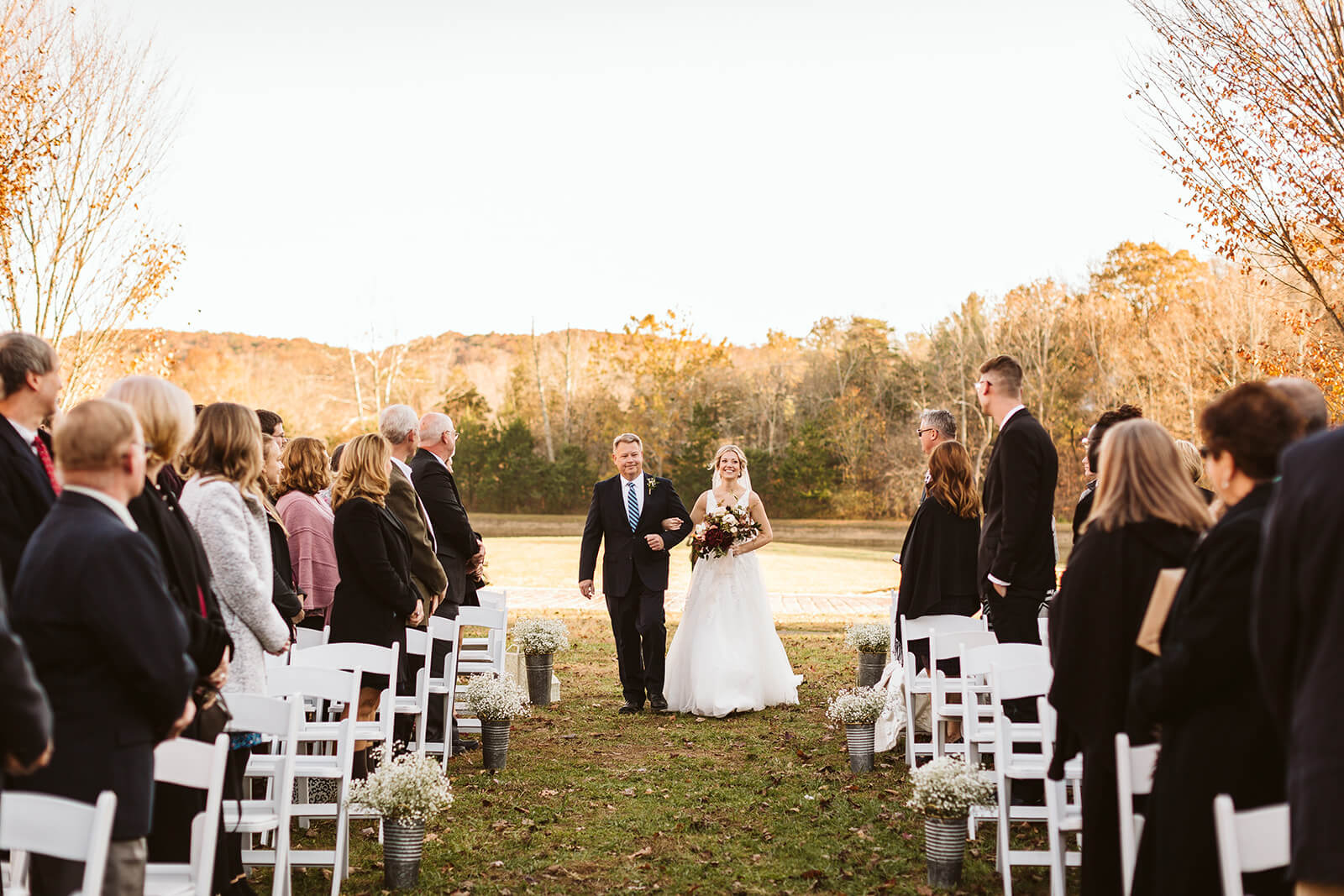 A bride and groom walk down the aisle together in an open field.