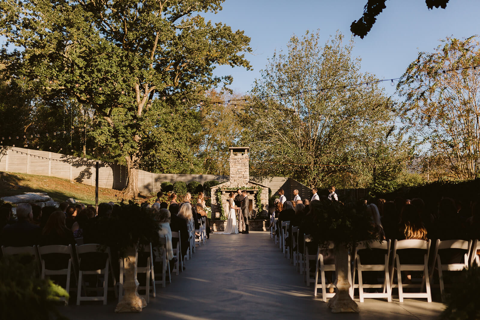 A bride and groom exchange vows in front of a freestanding outdoor fireplace.