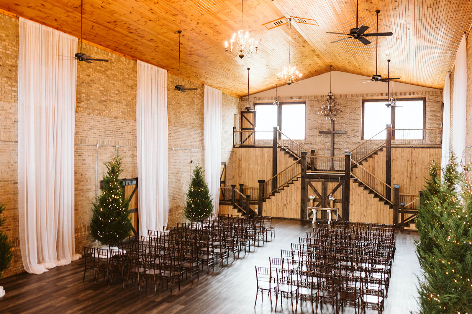 A wide shot of an empty wedding ceremony space. The altar is at the base of wood stairs beneath a large cross.