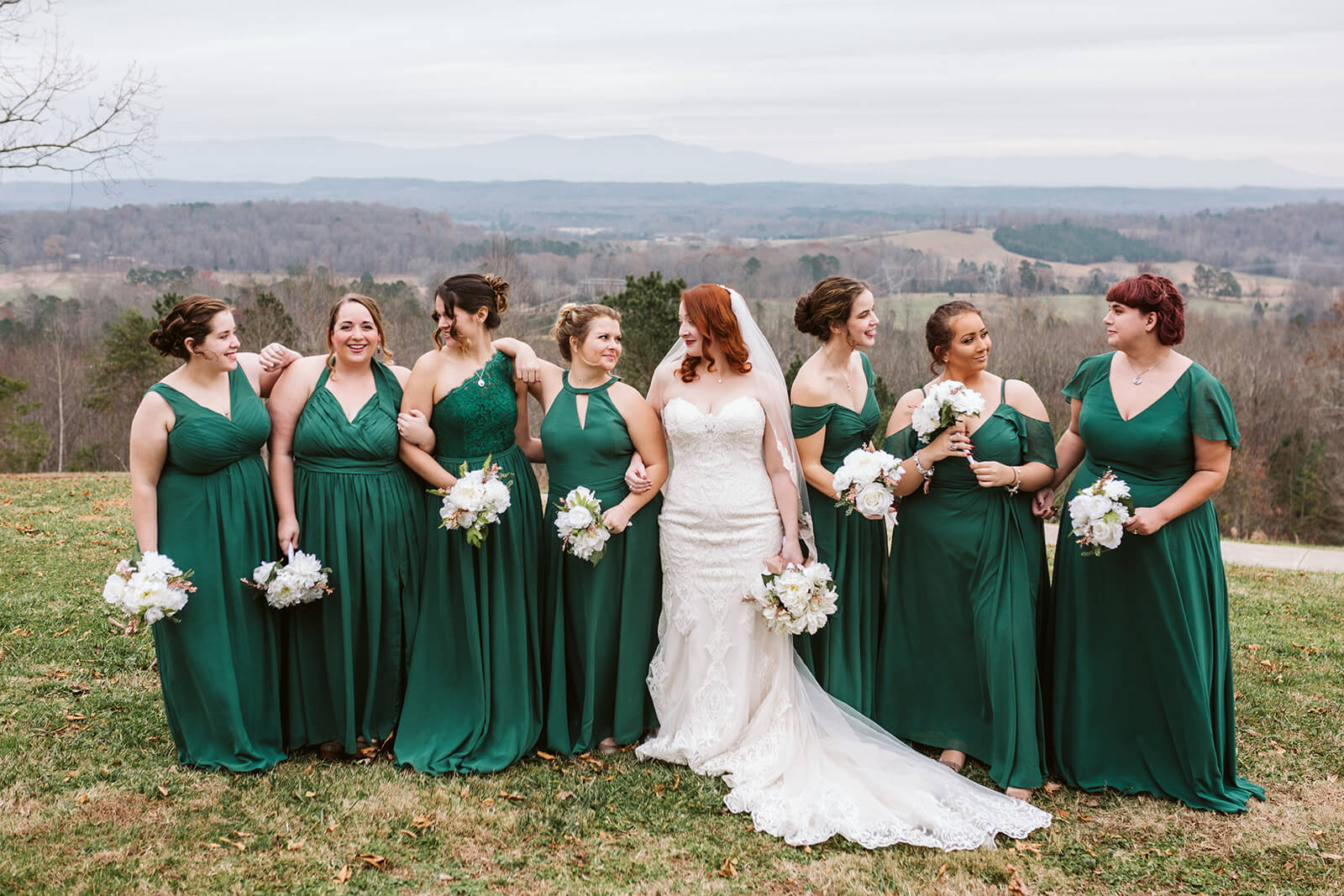 A bride poses with her bridesmaids, who are dressed in emerald green, in front of the hills at a mountain wedding venue in Chattanooga, TN.