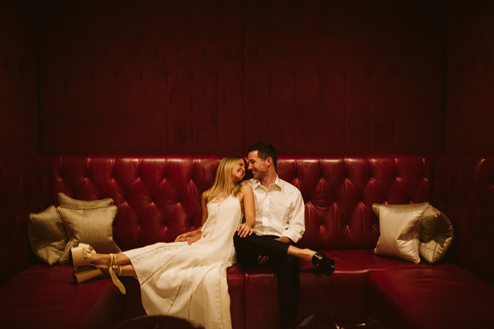 A couple lounges on a red leather sofa.