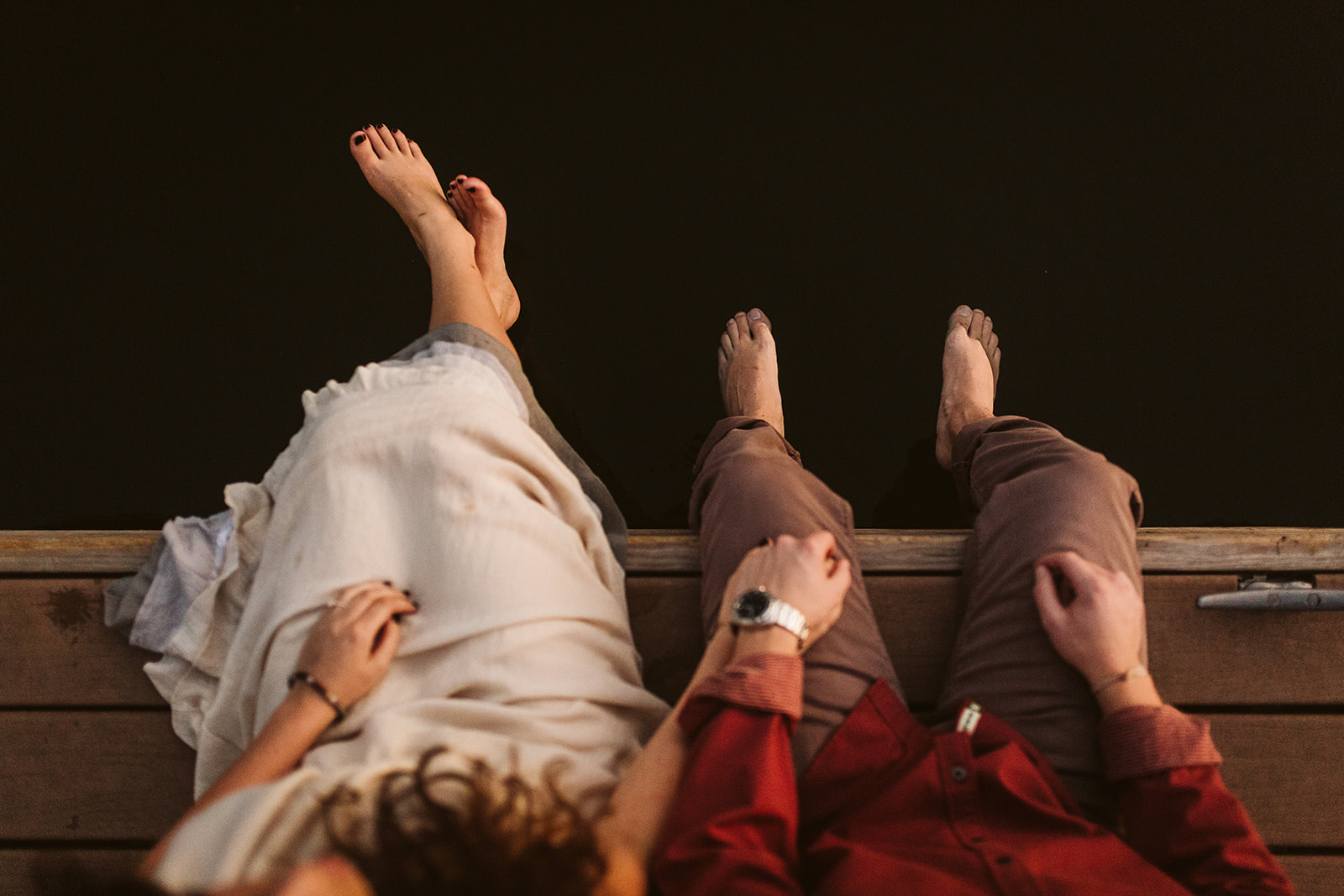 An overhead shot of a man and woman dangling their feet off a dock above a lake.