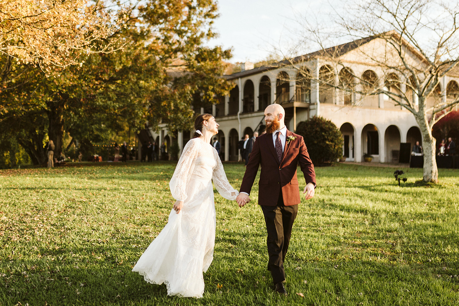 A bride and groom walk hand-in-hand across the lawn of their wedding venue.