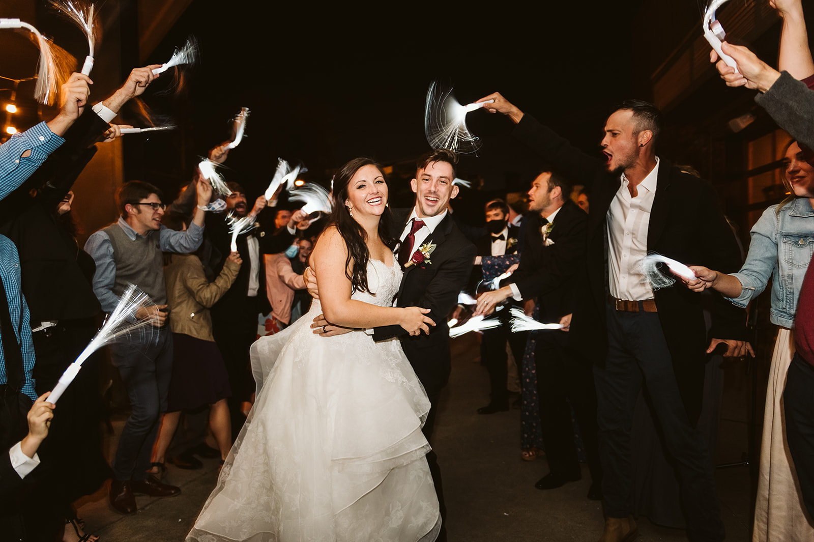 A bride and groom embrace under a glow stick exit at night.