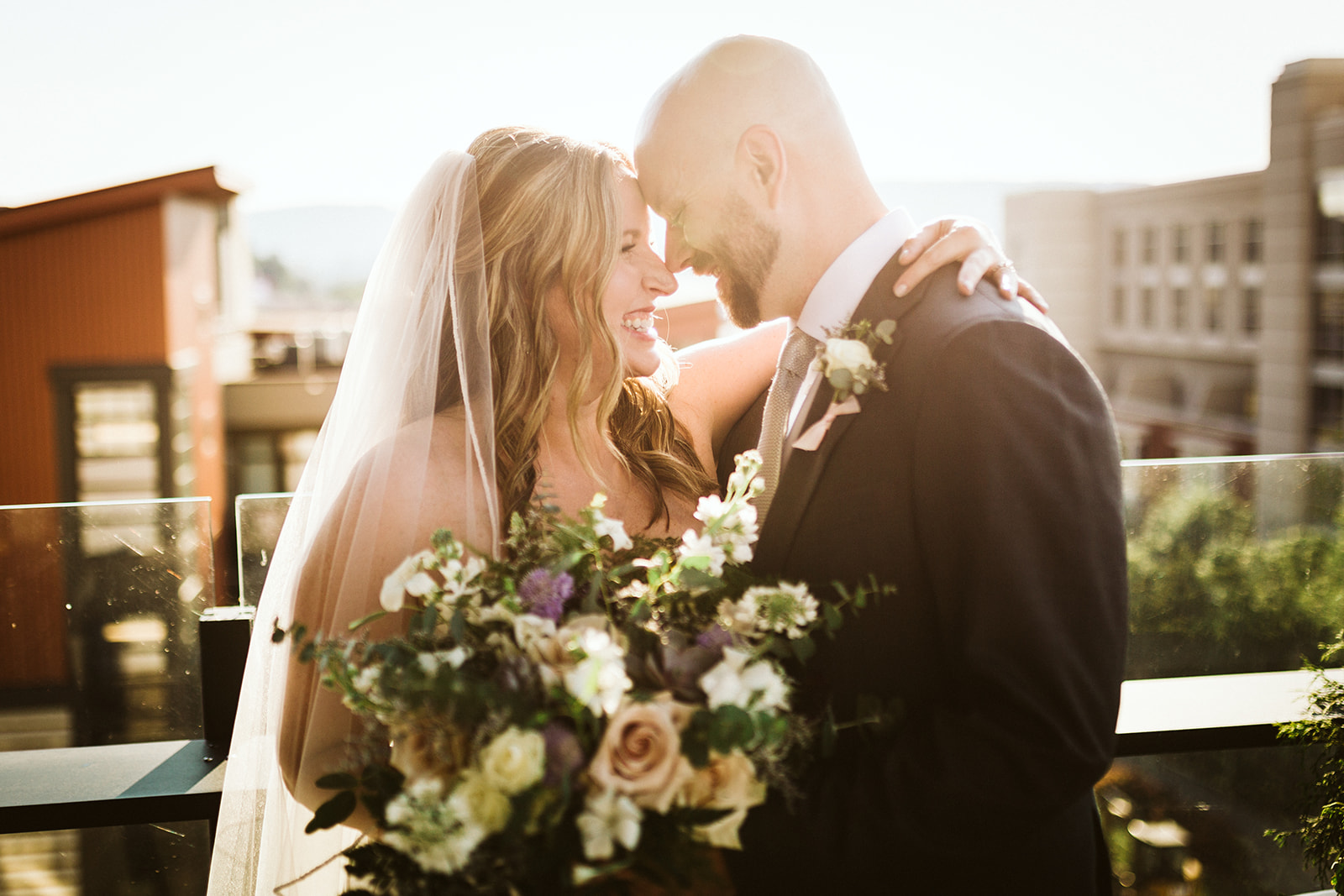 A bride and groom embrace in front of a city skyline.