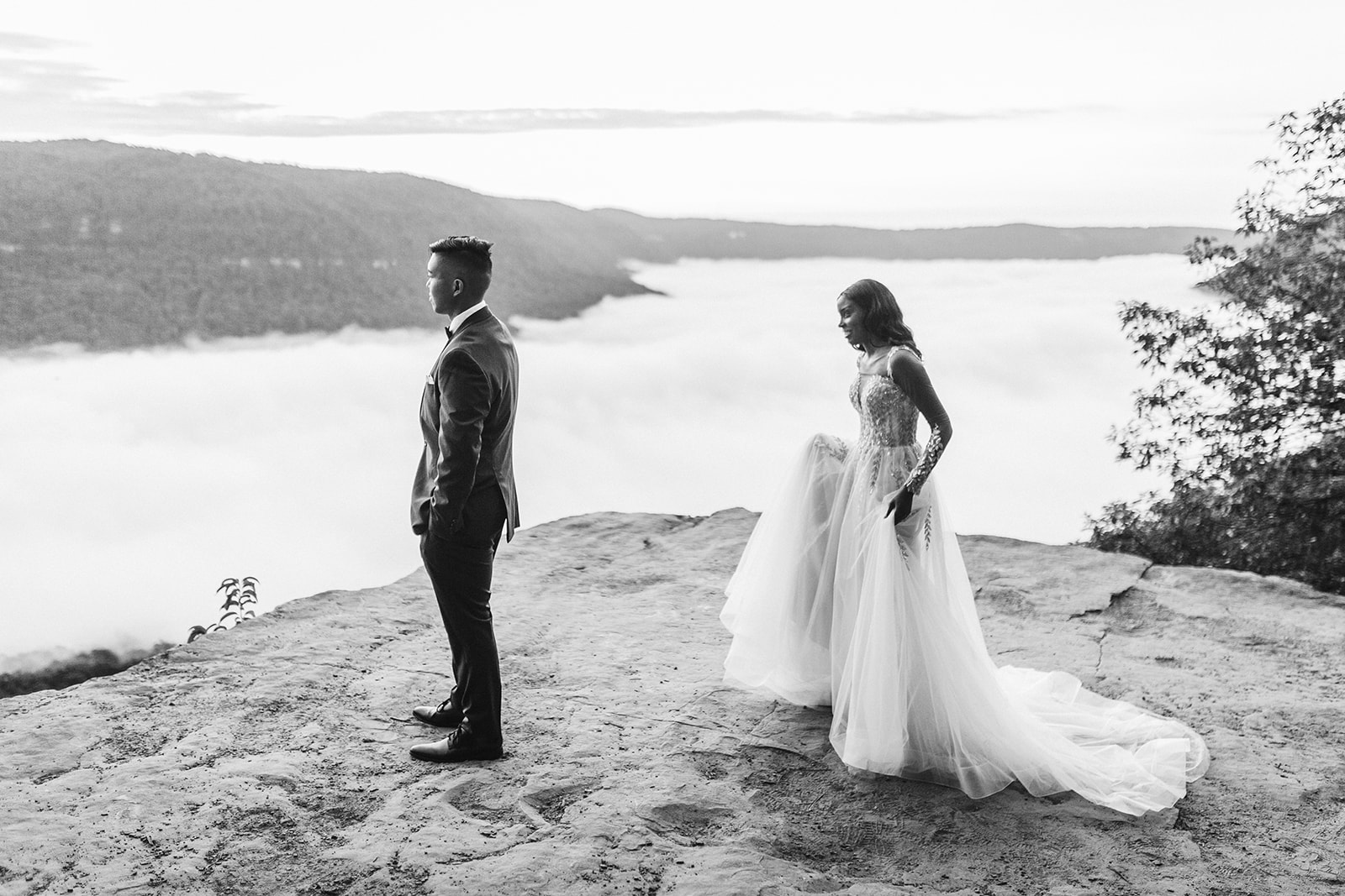 Bride approaches groom with his back to her on a mountain overlook during their engagement photo session near Chattanooga.