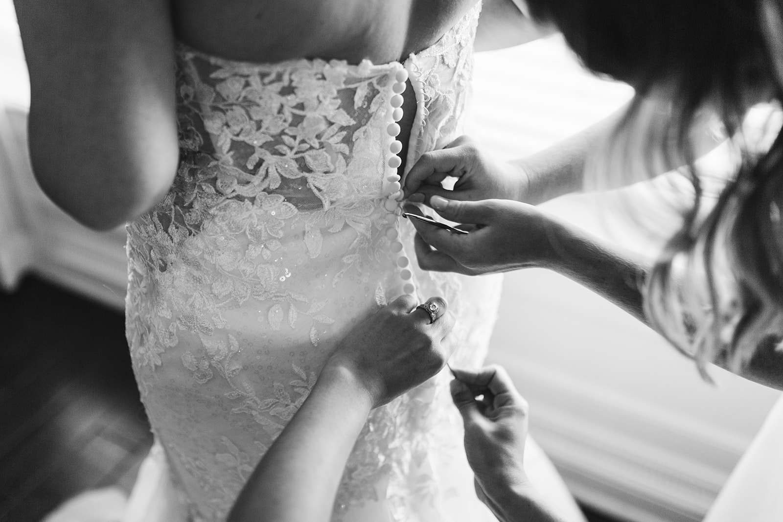 The bride's mother fastens the buttons on the back of her gown.