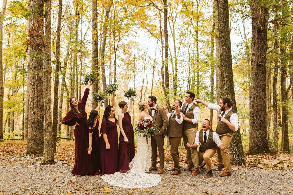 A bride and groom share a kiss as their wedding party celebrates on either side of them.