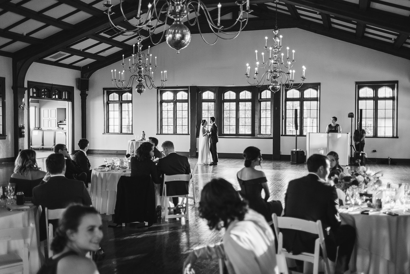 Black and white image of a bride and groom sharing their first dance while their wedding guests look on.