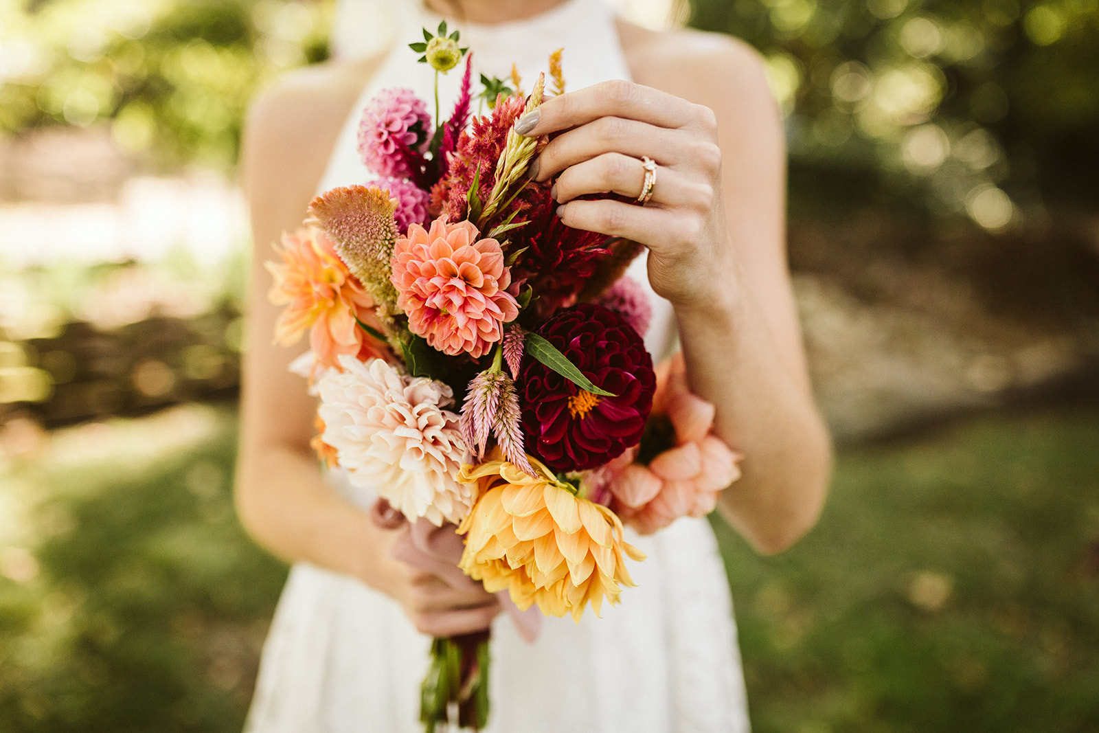 A bride examines her pink and red bouquet.