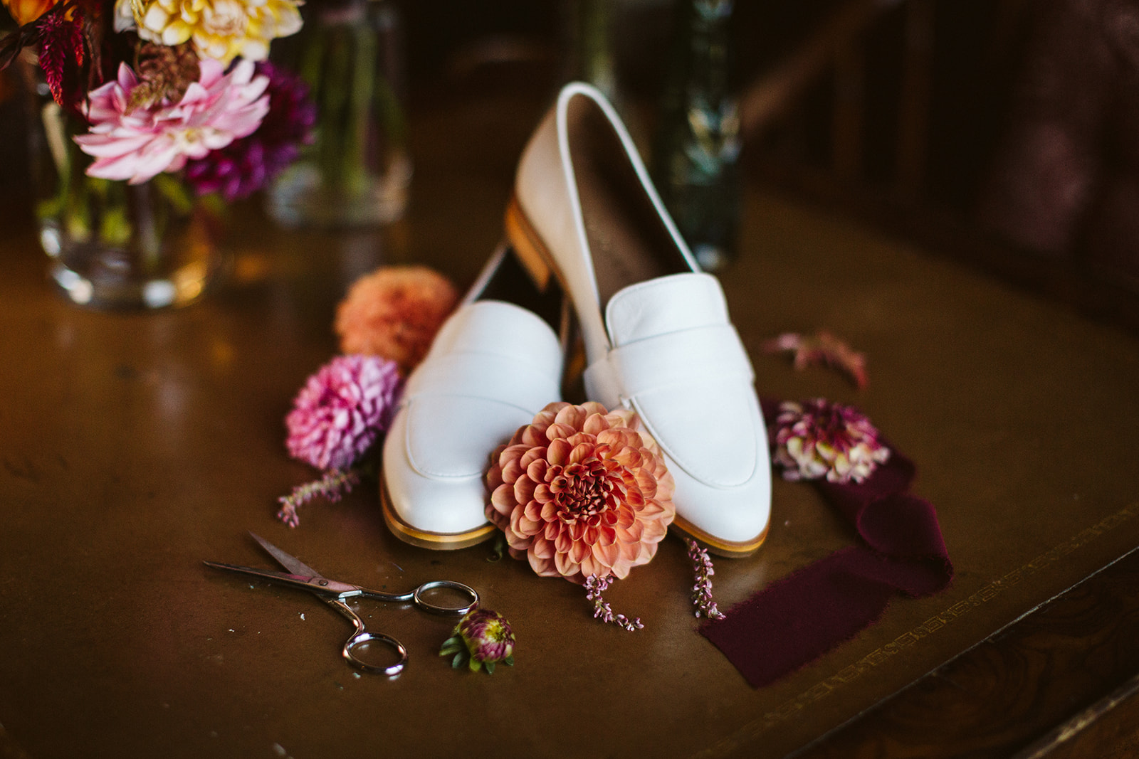 A pair of white women's dress shoes pictured amidst red and pink flowers.