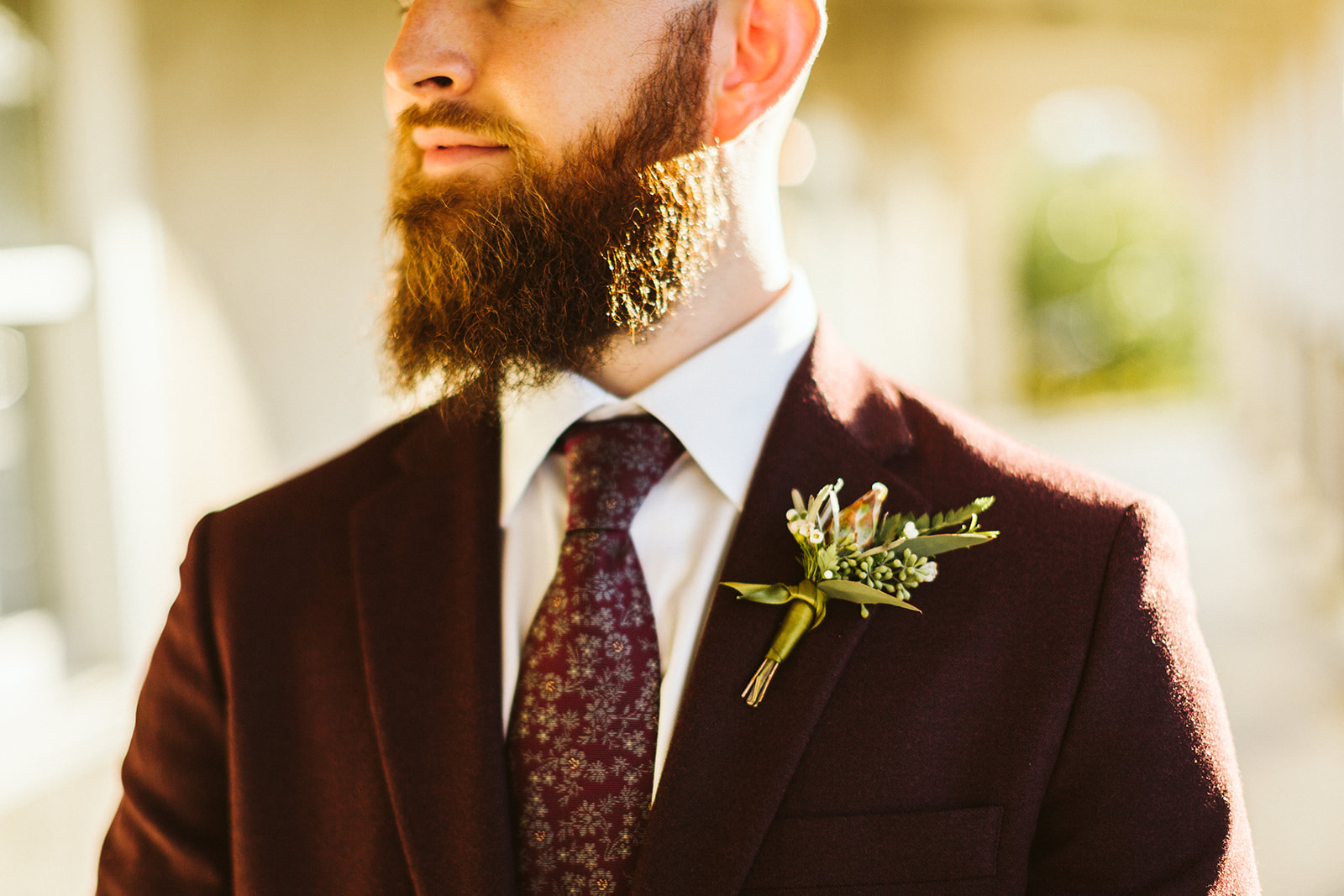 Close up of the grooms boutonniere pinned on his maroon suit coat