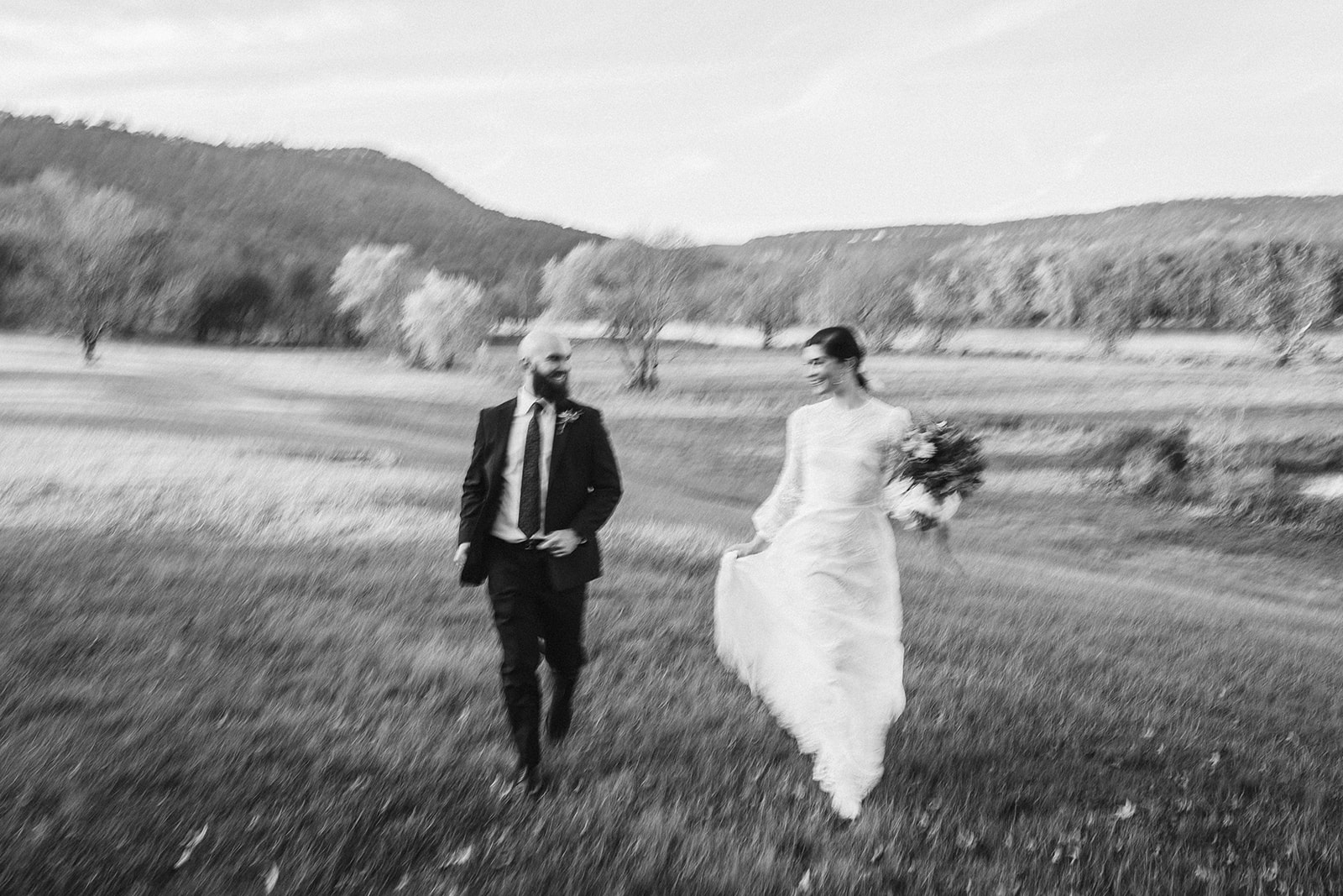 Blurry black and white photo of the bride and groom laughing as they run through a field outside their wedding at the Tennessee Riverplace